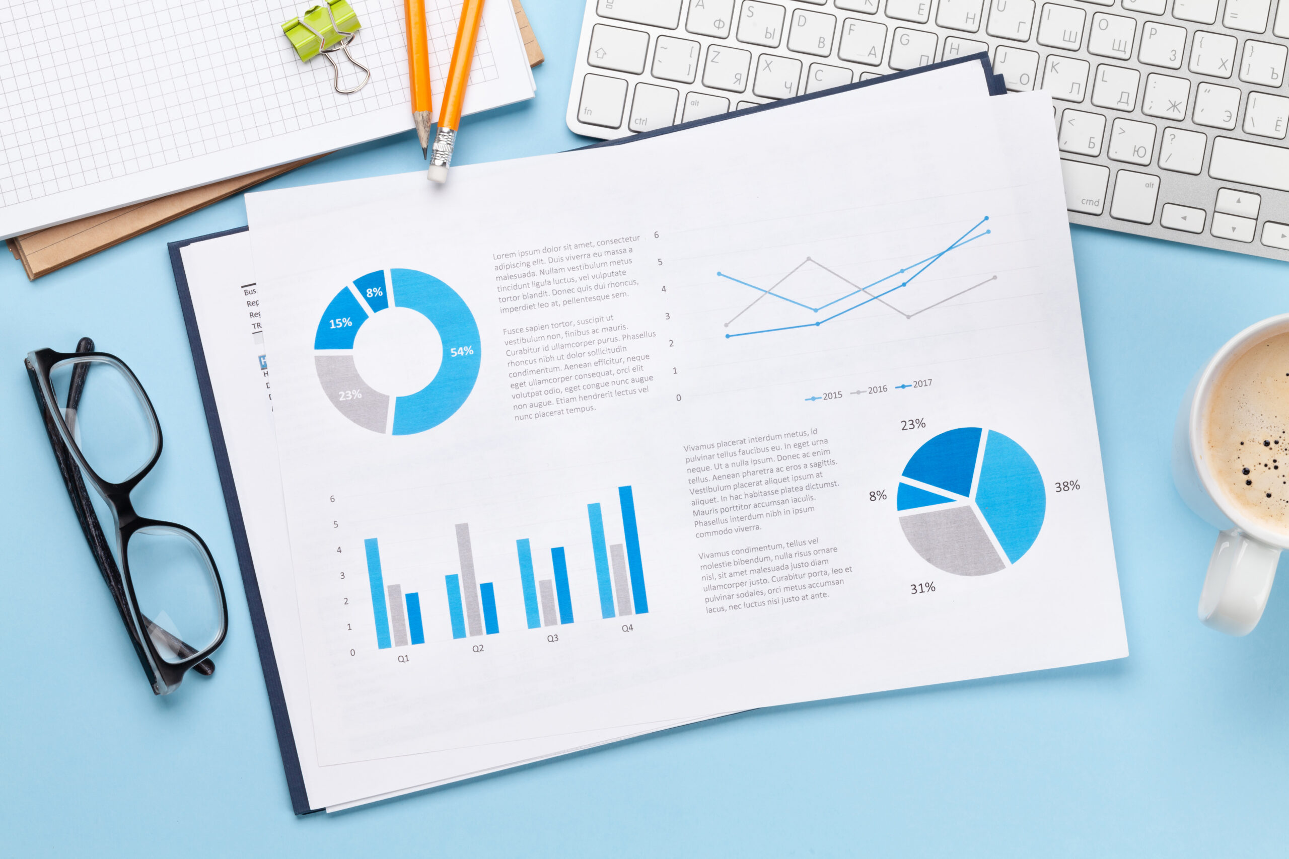 A desk with a keyboard, eyeglasses, a cup of coffee, and a sheet featuring blue and gray charts and graphs for a step-by-step guide to long-term digital success.