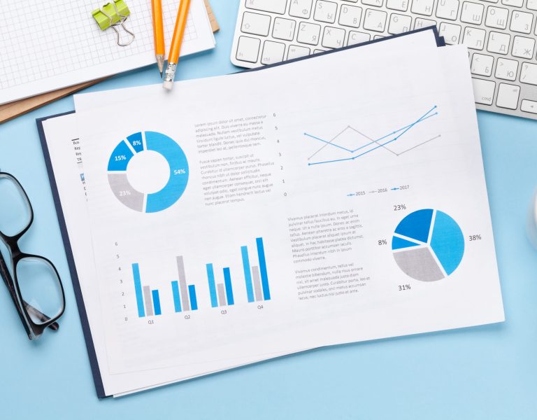 A desk with a keyboard, eyeglasses, a cup of coffee, and a sheet featuring blue and gray charts and graphs for a step-by-step guide to long-term digital success.